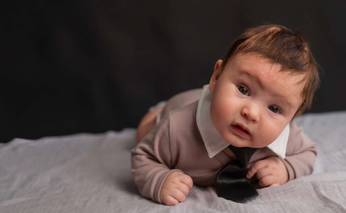 Bambino sdraiato con body elegante e cravatta, simbolo di stile e originalità nei nomi maschili italiani che iniziano con la lettera I