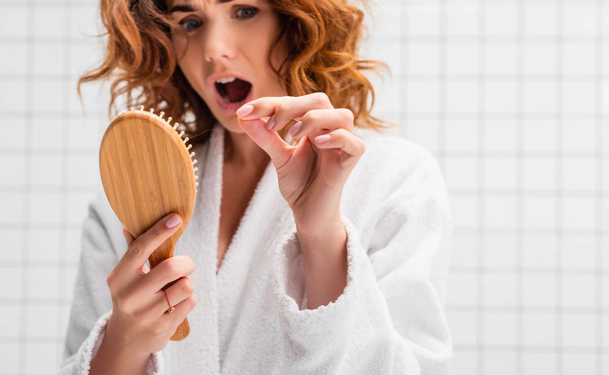 Donna preoccupata osserva una spazzola piena di capelli dopo la pettinatura, segnale visibile di caduta eccessiva dei capelli