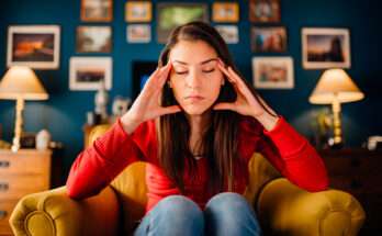 Donna seduta su una poltrona con gli occhi chiusi e le mani alle tempie, in un momento di sovraccarico mentale e pensieri ossessivi nella routine quotidiana.