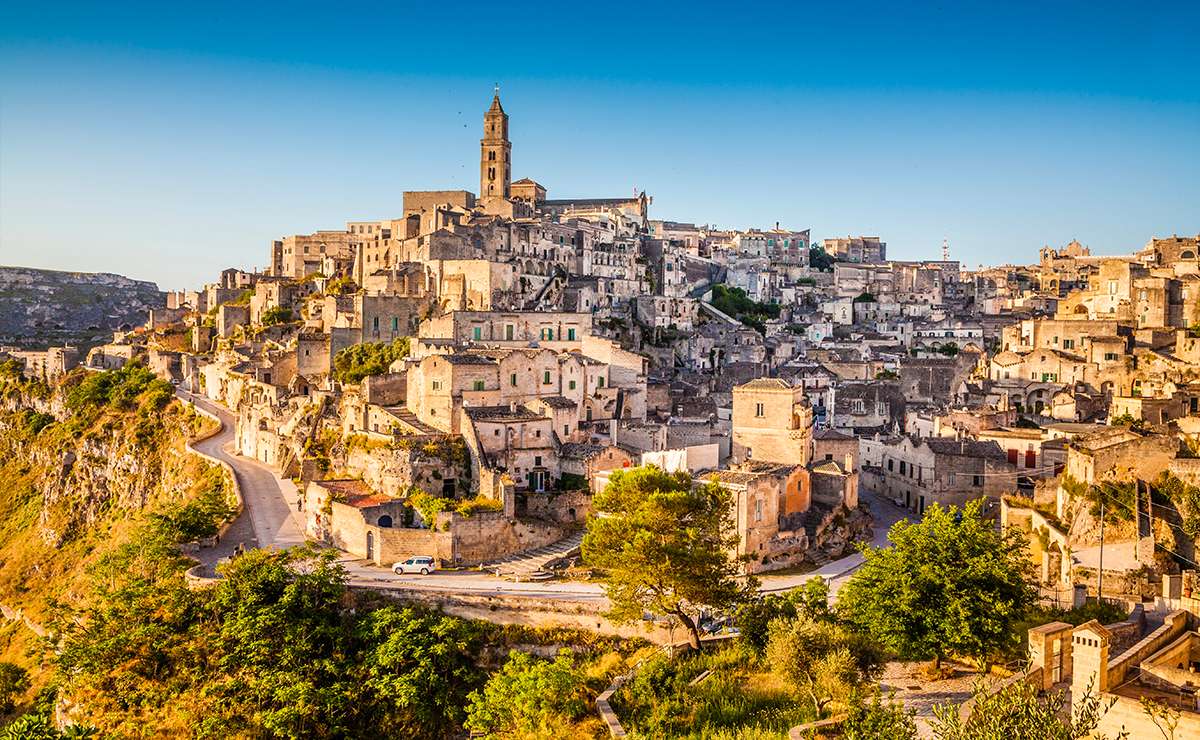 Panorama dei Sassi di Matera al tramonto, con le antiche abitazioni in pietra arroccate sulla collina e il campanile della Cattedrale sullo sfondo.