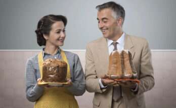 Coppia elegante con panettone e pandoro in mano, sorridenti in cucina anni ’50: confronto tra i due dolci natalizi tradizionali italiani.