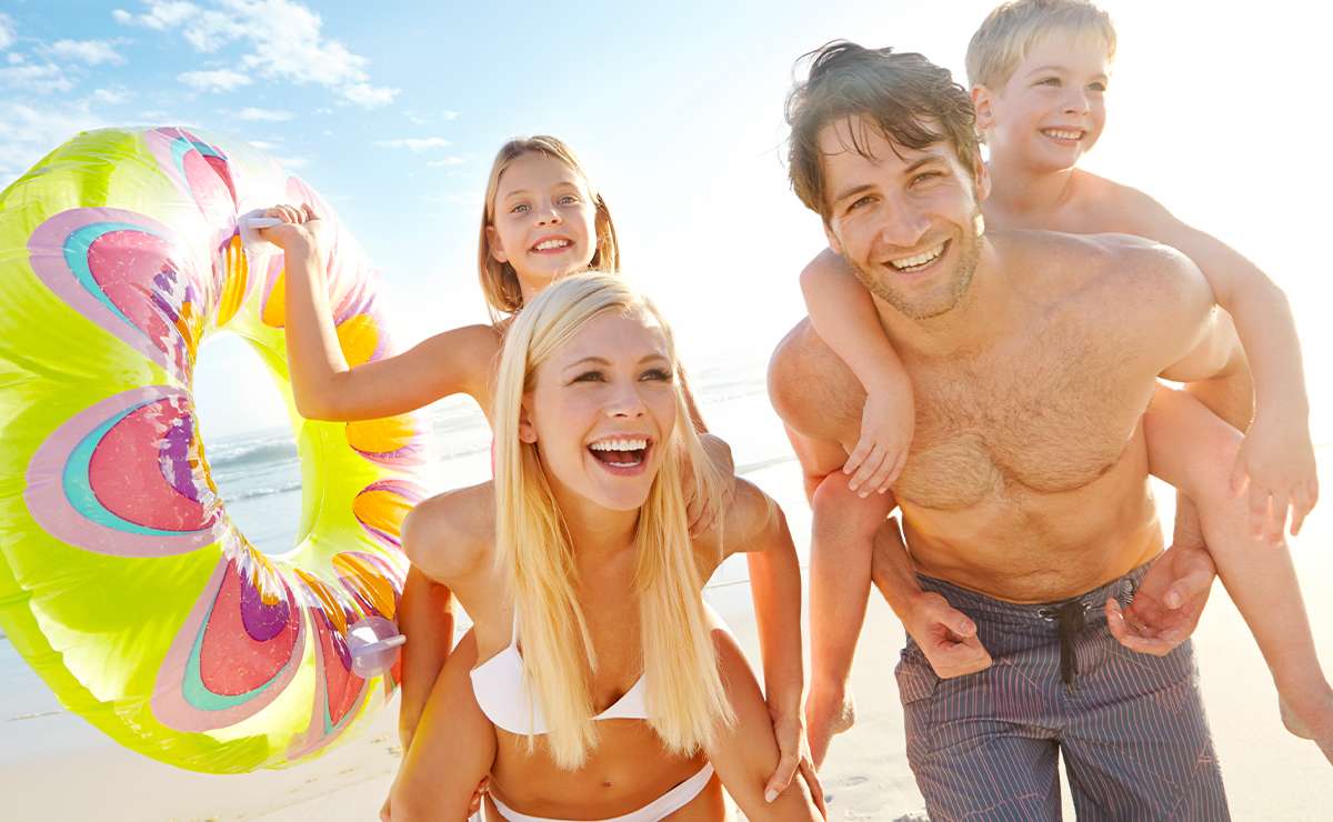 Famiglia sorridente in spiaggia con due bambini, salvagente colorato e mare sullo sfondo: vacanze estive in Campania a misura di bambini.
