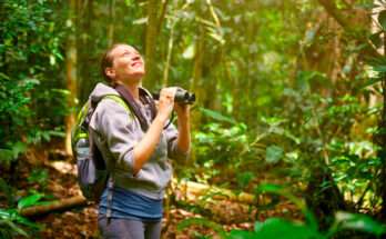 Donna con zaino e binocolo che osserva gli uccelli in una foresta tropicale, durante un’escursione di birdwatching immersa nella natura.