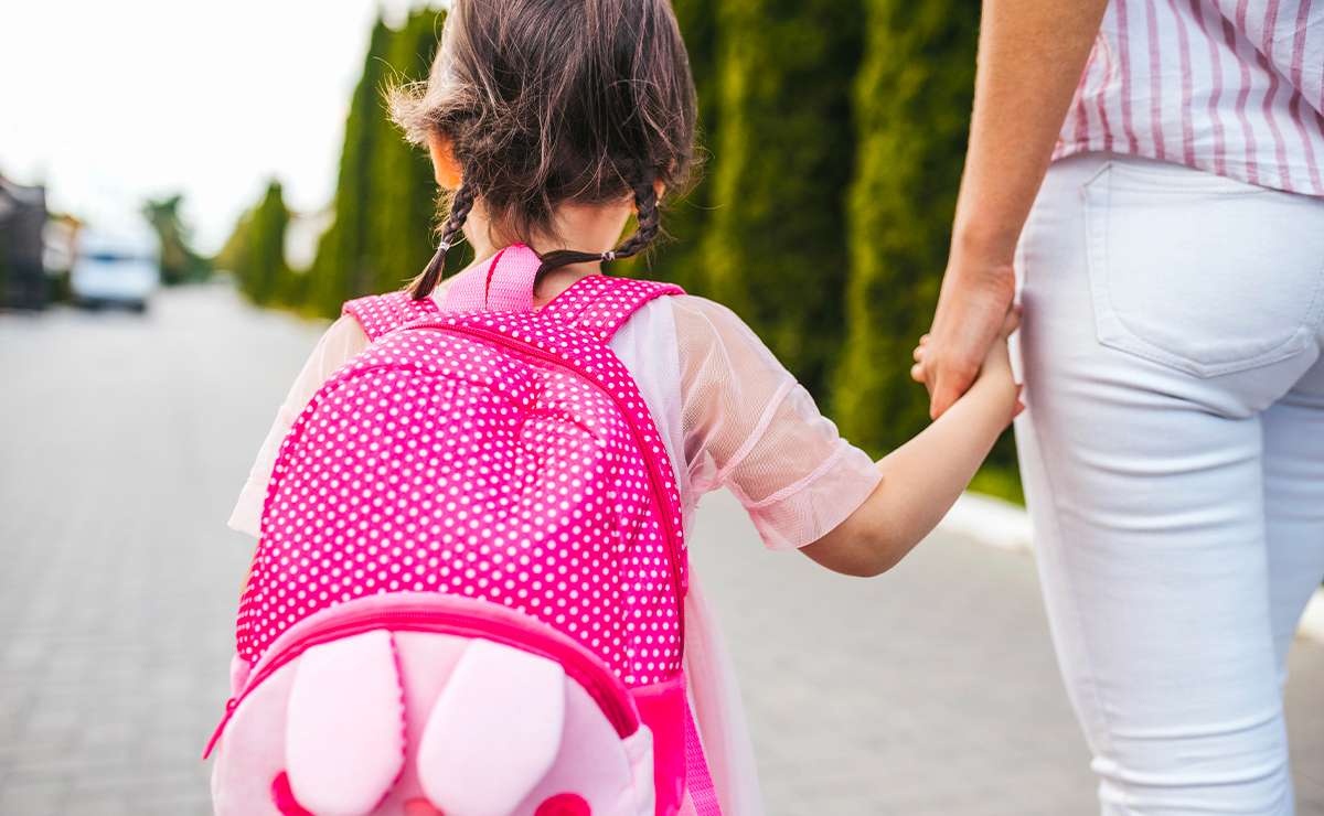 Bambina con zaino rosa a pois, mano nella mano con la mamma, mentre si avvia al primo giorno di scuola.
