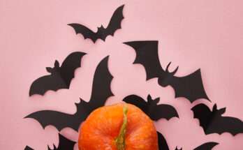 Decorazione di Halloween con pipistrelli neri in carta su sfondo rosa e una zucca arancione in primo piano