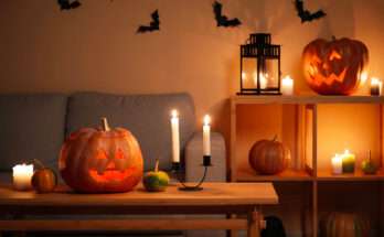 Soggiorno decorato per Halloween con zucche intagliate illuminate, candele accese e pipistrelli neri alle pareti, atmosfera calda e spettrale.