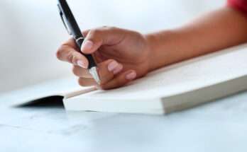 Mano femminile che scrive una dedica su un libro aperto, idea per regalo personalizzato con messaggio scritto a mano.