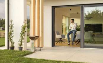 Uomo accanto a una grande vetrata scorrevole in una casa con vista giardino