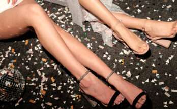 Due donne con sandali eleganti posano su un pavimento coperto di coriandoli e frammenti dorati, atmosfera da festa notturna