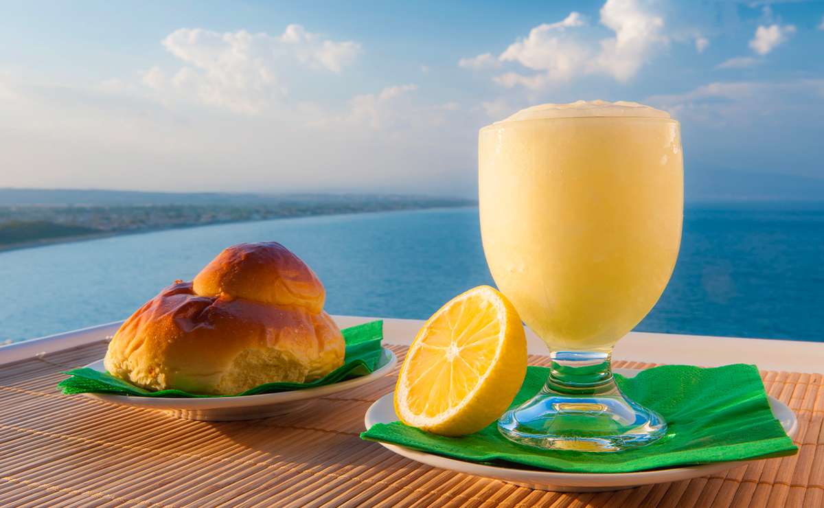 Granita siciliana al limone con brioscia col tuppo servita vista mare, tipica colazione estiva siciliana.