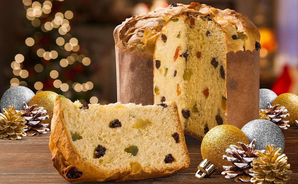 Panettone tradizionale tagliato a fette con canditi e uvetta, decorazione natalizia sul tavolo e albero di Natale sfocato sullo sfondo.