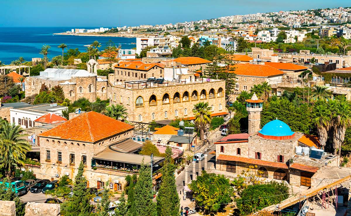 Panorama della città storica di Byblos in Libano, con edifici in pietra, tetti rossi, minareto con cupola blu e vista sul Mar Mediterraneo.
