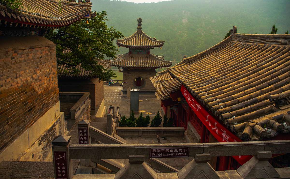 Tempio tradizionale cinese a Luoyang, una delle città più antiche del mondo, con tetti in tegole gialle e vista sulle montagne nebbiose.
