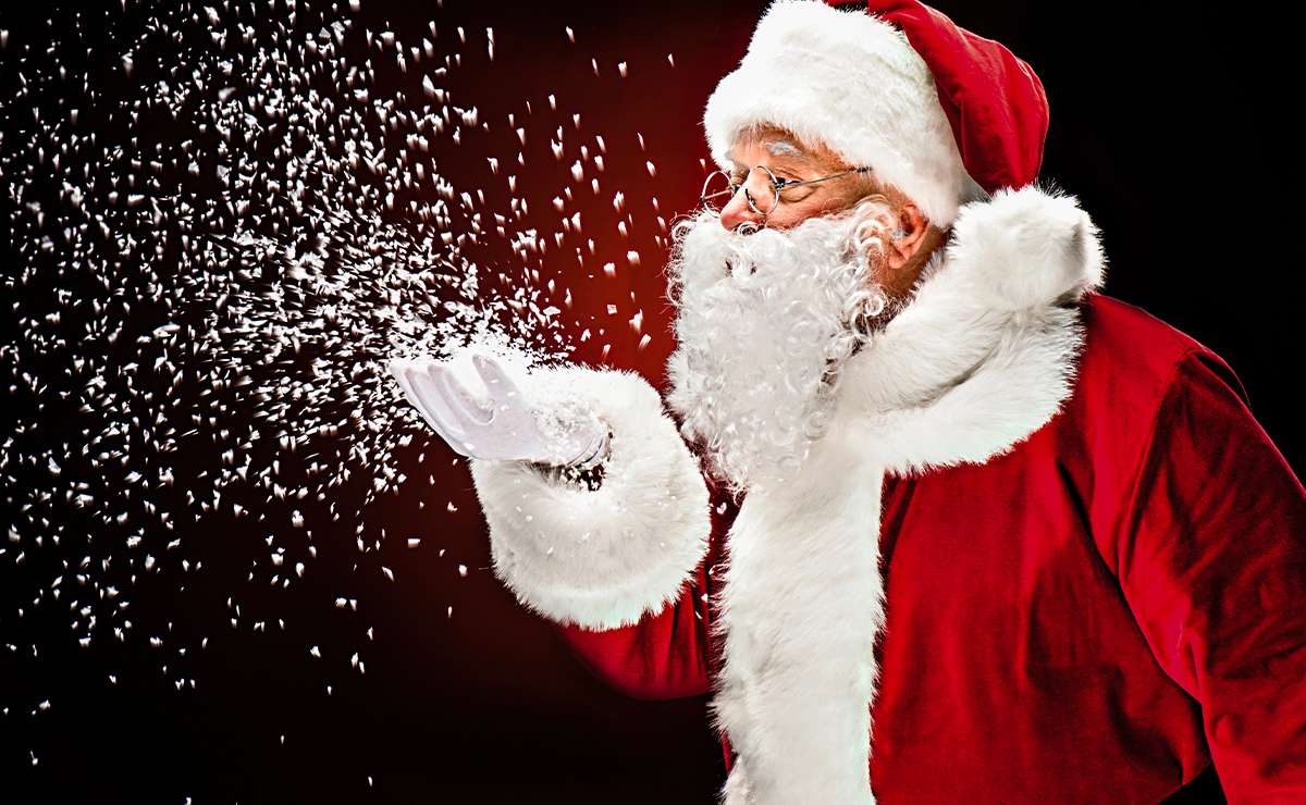 Babbo Natale con abito rosso e barba bianca soffia fiocchi di neve, simbolo delle feste natalizie.