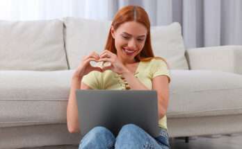 Ragazza che sorride davanti al computer facendo un cuore con le mani
