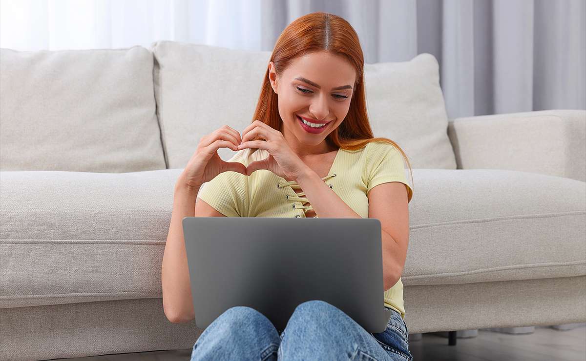 Ragazza che sorride davanti al computer facendo un cuore con le mani