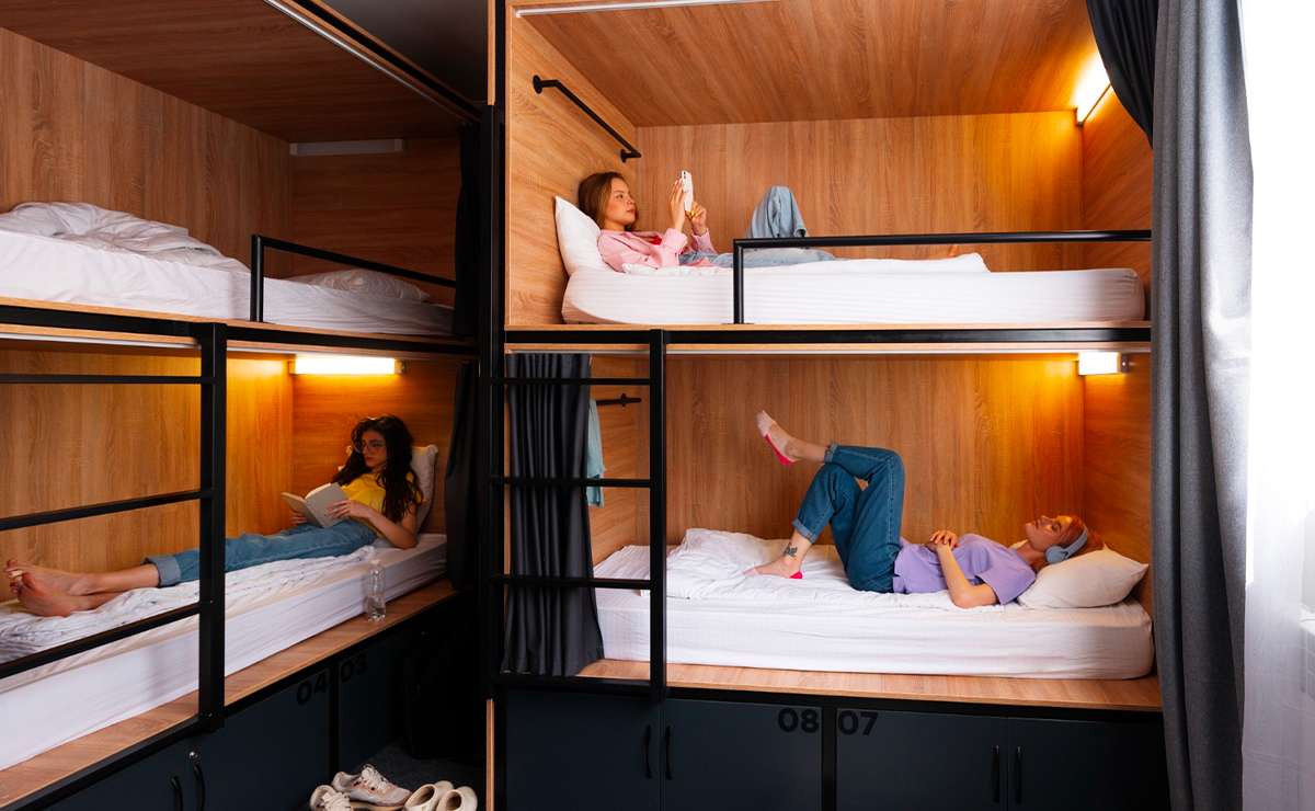 Letti a castello in legno con luci e tende, ragazze rilassate in una stanza condivisa.
