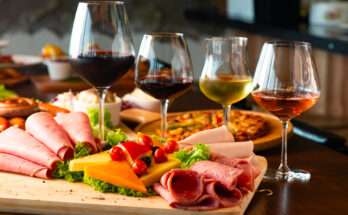 Tagliere di salumi e formaggi con pomodorini e insalata, accompagnato da calici di vino rosso