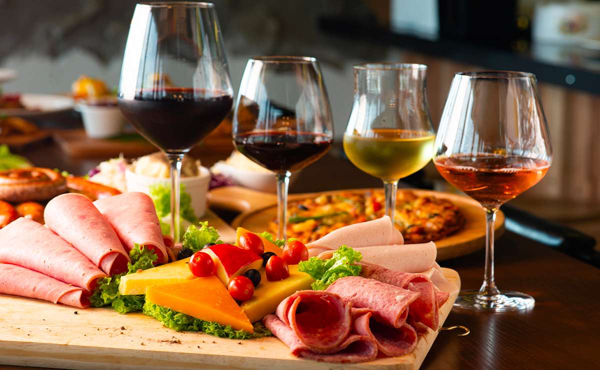 Tagliere di salumi e formaggi con pomodorini e insalata, accompagnato da calici di vino rosso