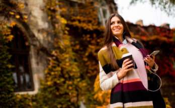 Donna con sciarpa a righe colorate, cappotto chiaro e caffè takeaway