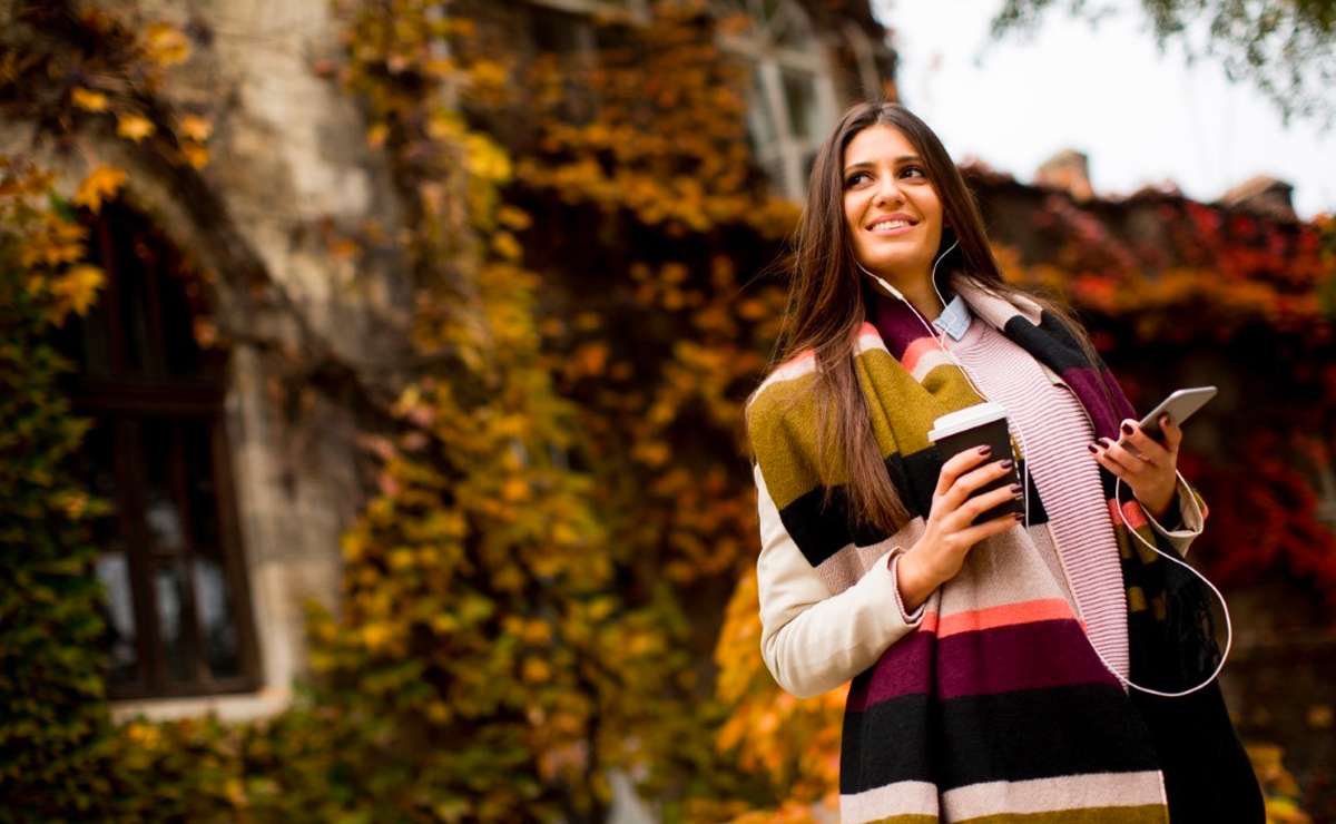 Donna con sciarpa a righe colorate, cappotto chiaro e caffè takeaway