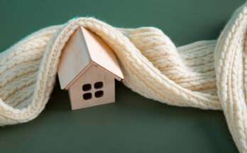 Casa in legno avvolta da una sciarpa di lana, simbolo di comfort termico domestico.