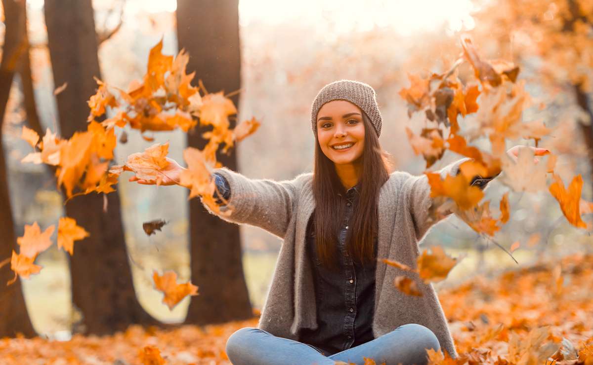Ragazza sorridente in un parco d’autunno lancia foglie colorate, simbolo dell’inizio dell’autunno e del foliage di settembre.