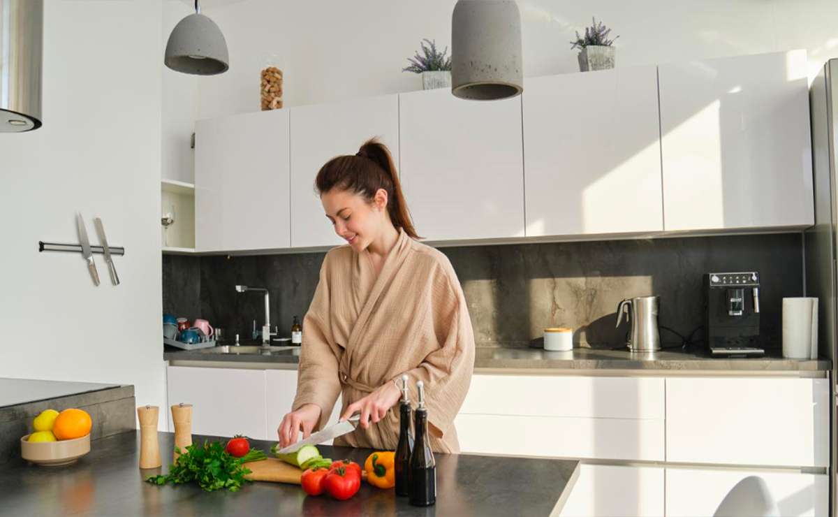 Donna che prepara verdure in una cucina moderna con mobili bianchi e piano in cemento