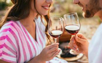 Coppia che brinda con due calici di vino rosso durante un tramonto estivo