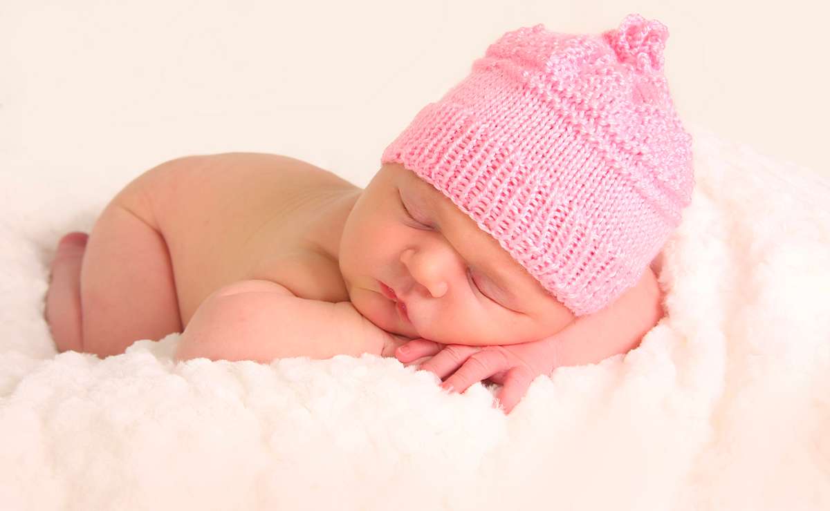 Neonata che dorme avvolta in una coperta bianca e indossa un cappellino rosa