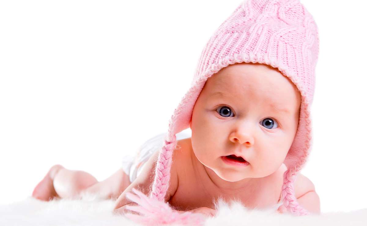 Bambina con cuffia rosa sdraiata su una coperta bianca