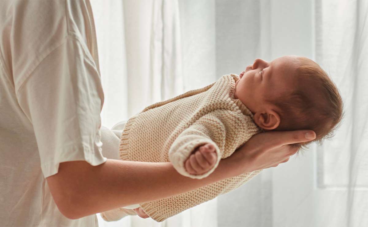 Neonato in braccio alla madre vicino a una finestra con luce naturale
