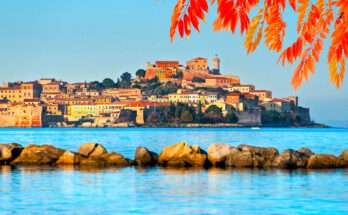 Veduta autunnale dell’Isola d’Elba con il borgo di Portoferraio illuminato dal sole e foglie colorate in primo piano