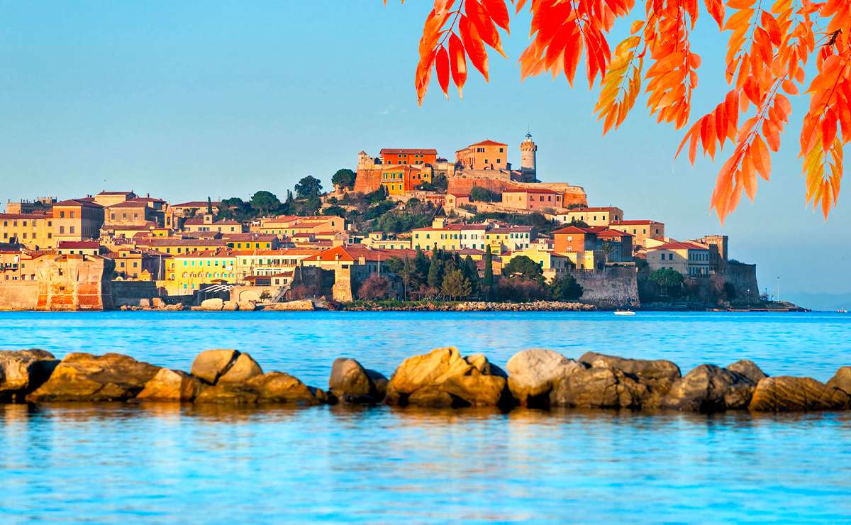 Veduta autunnale dell’Isola d’Elba con il borgo di Portoferraio illuminato dal sole e foglie colorate in primo piano