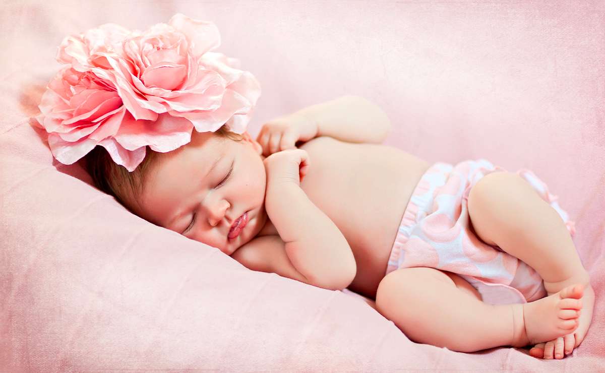 Neonata che dorme su una copertina rosa con un grande fiore rosa sulla testa.
