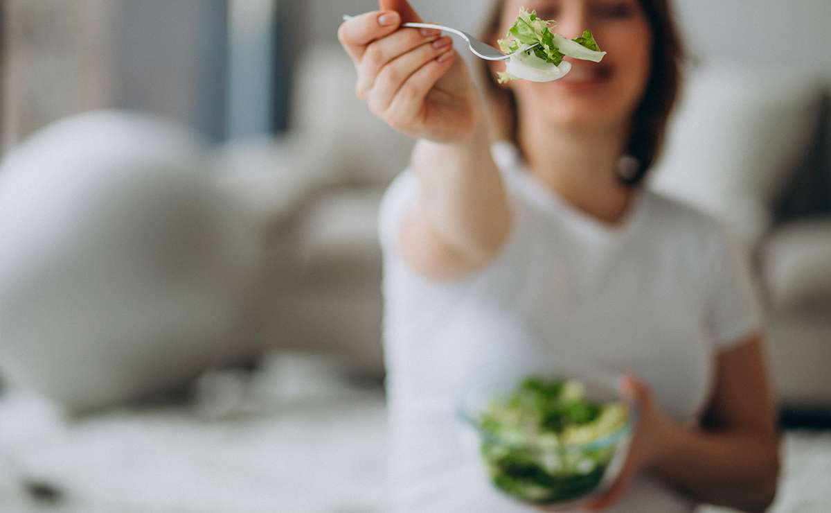 Persona che porge una forchetta con insalata fresca