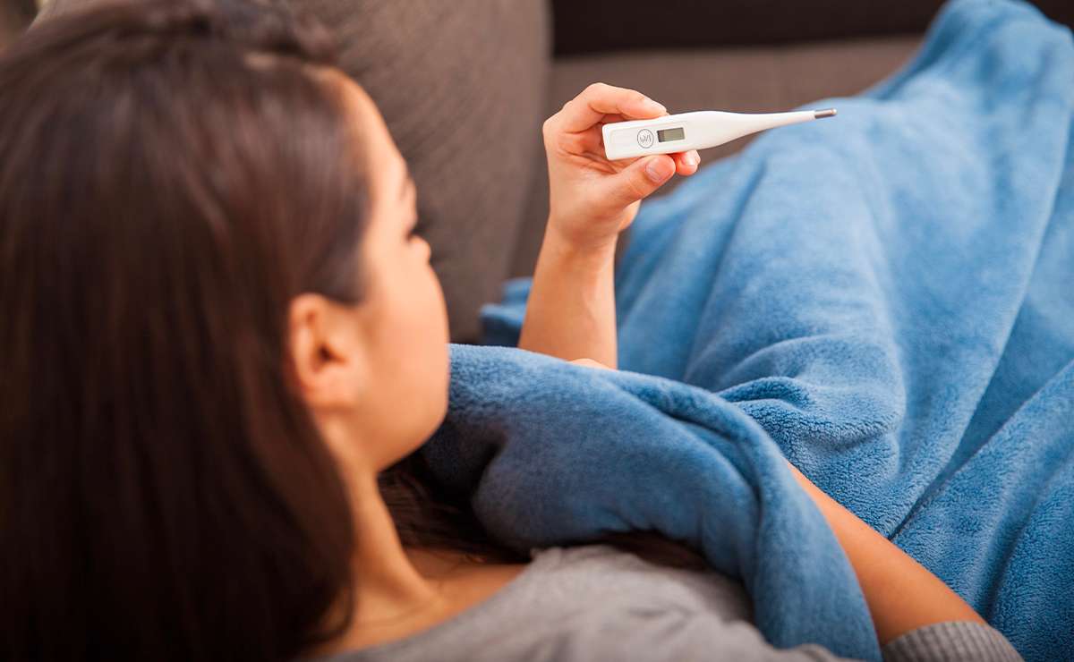 Donna a letto con una coperta blu mentre controlla la temperatura su un termometro