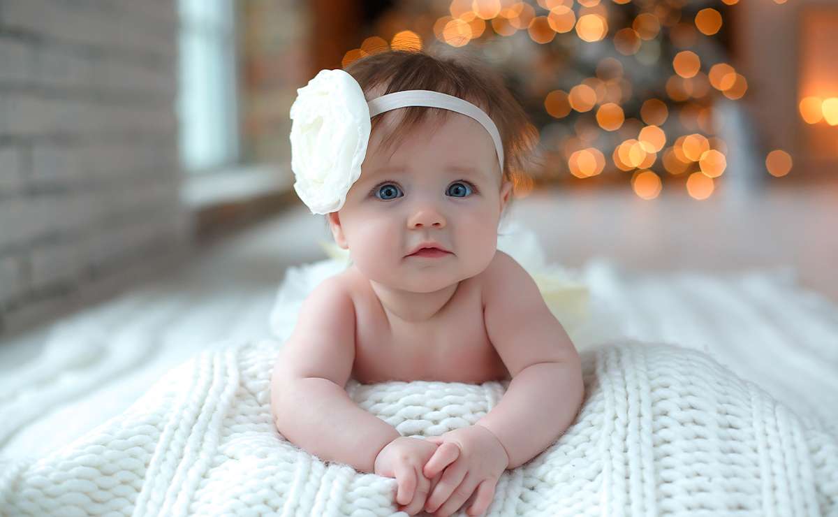 Bambina con fascia bianca e grande fiore mentre è distesa su una coperta morbida