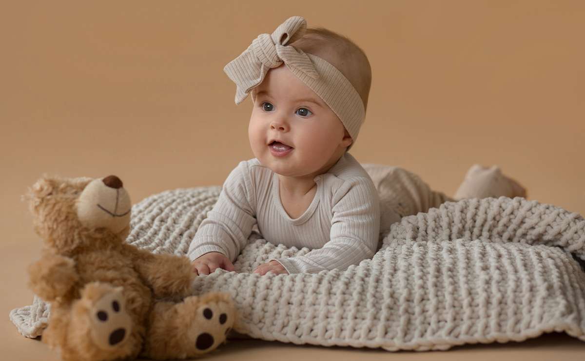 Bambina che sorride mentre è sdraiata su una coperta color panna