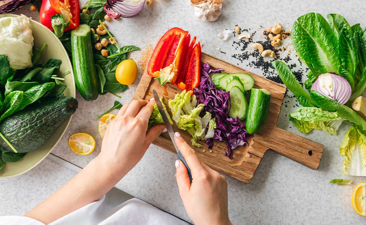 Mani che affettano verdure fresche su un tagliere di legno