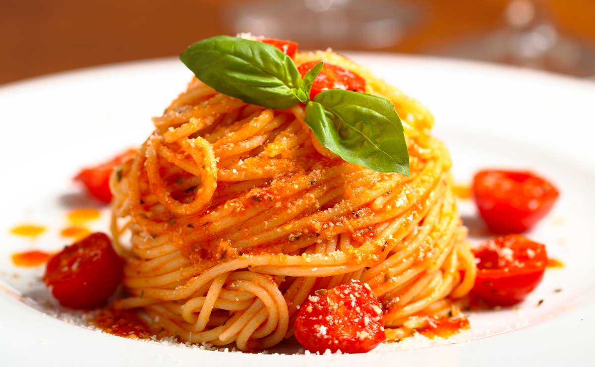 Spaghetti al pomodoro con basilico fresco serviti su un piatto bianco, con pomodorini e formaggio grattugiato