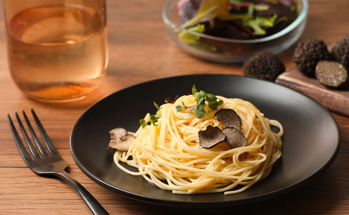 Spaghetti gourmet al tartufo serviti su piatto nero con scaglie di tartufo fresco e germogli