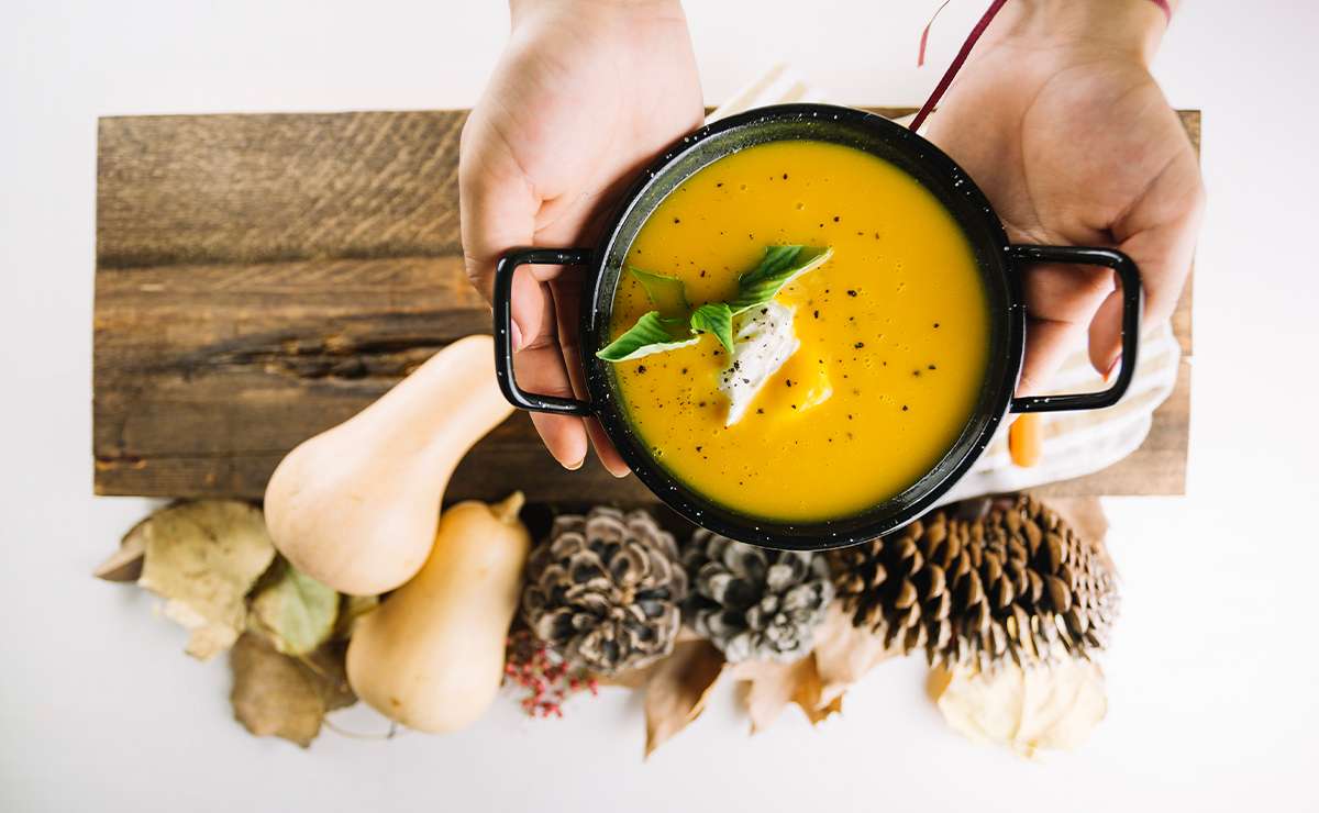 zuppa cremosa arancione servita in una ciotola nera con erbe fresche