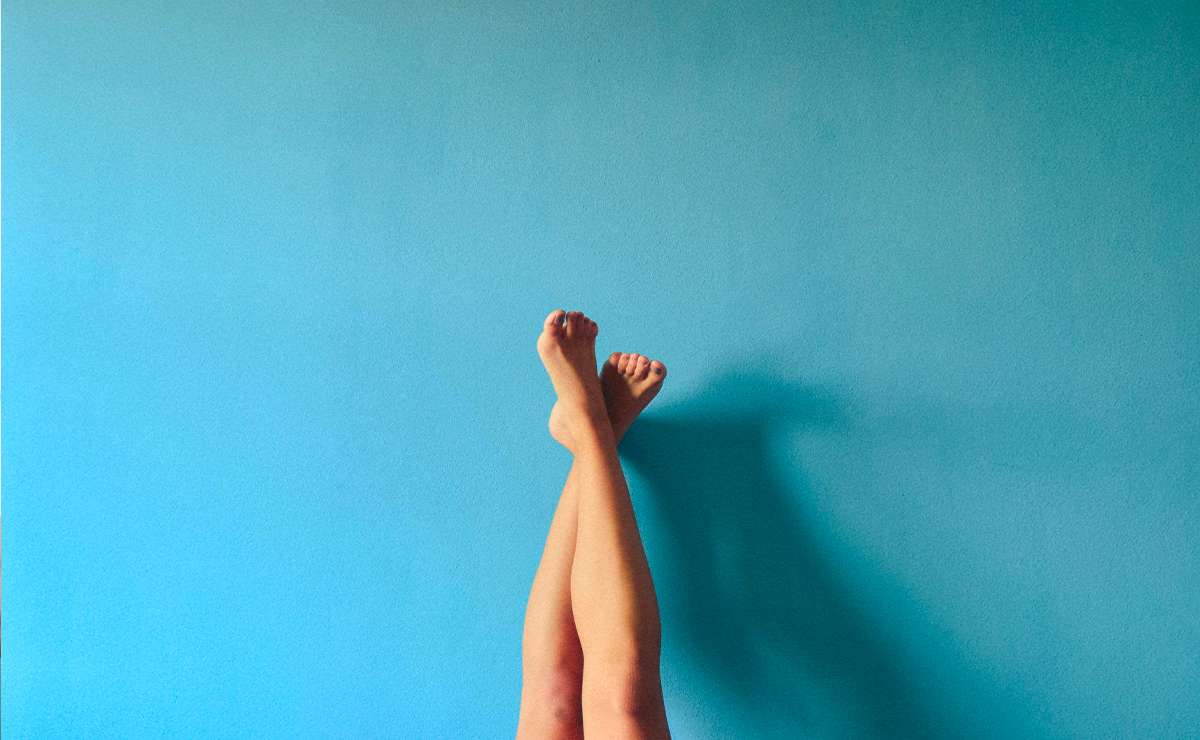 Gambe depilate sollevate contro una parete azzurra