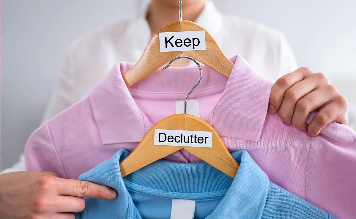 Persona che tiene due grucce con maglie colorate, una etichettata “Keep” e una “Declutter”