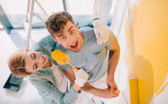 Coppia che dipinge una parete di casa con rullo giallo