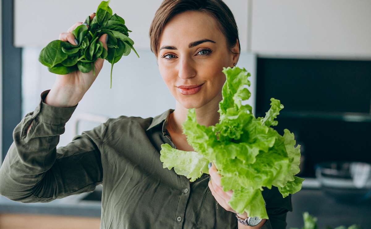 Donna in cucina che tiene in mano foglie di spinaci e lattuga fresca