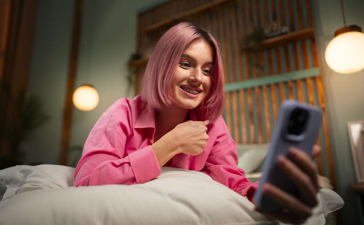 Ragazza sul letto con smartphone in mano che sorride mentre invia un messaggio della buonanotte