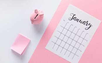 Calendario di gennaio appoggiato su un foglio rosa accanto a un salvadanaio rosa