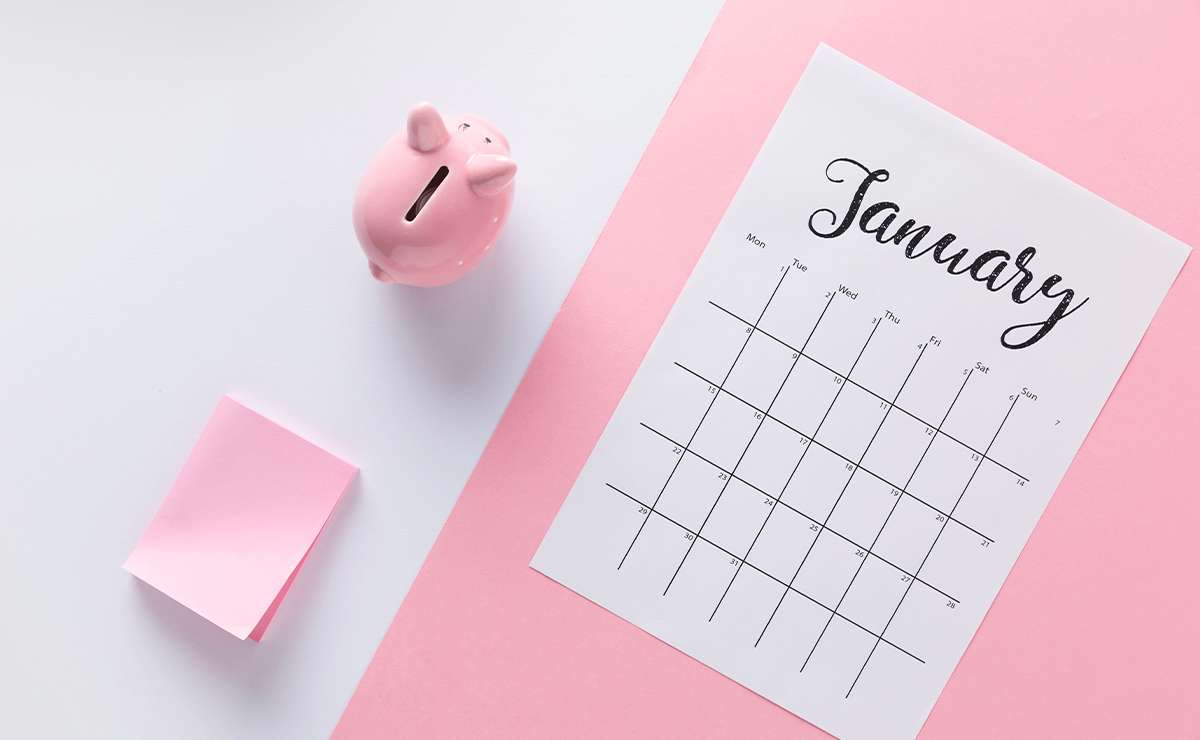 Calendario di gennaio appoggiato su un foglio rosa accanto a un salvadanaio rosa